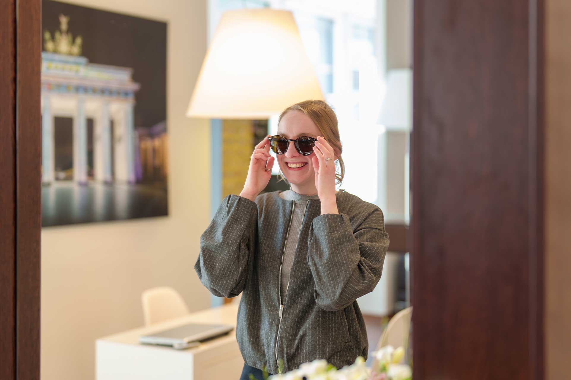 Wolff-Optic-0326_Charlene-Hartisch-Anprobe Links ein Mann, welcher von einer Frau auf der rechten Seite verschiedene Brillen zur Probe auf einem Tablett gereicht bekommt.